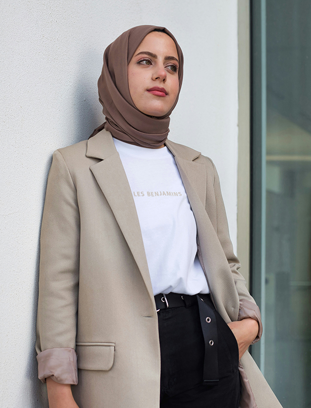 Eine junge, modern angezogene Frau mit einem schicken Blazer und mit Hijab schaut in die Ferne